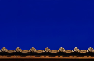 Japanese traditional grey roof tile with old spiral motif and blue sky above as background (with copy space)
