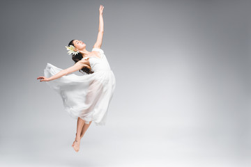graceful ballerina in white dress jumping while dancing on grey background © LIGHTFIELD STUDIOS