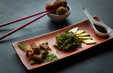 Gebratener Tofu auf Holzplatte mit Gemüse, Sauce und Avocado mit Falafel und Stäbchen auf  dunklen Hintergrund - 285518472