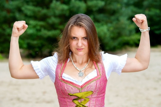 young woman in dirndl standing outdoors and flexing her muscles