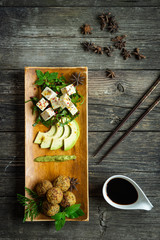 Tofu mit frischem Gemüse, Avocado und Gewürzen auf Teller und Holztisch, Ansicht von oben