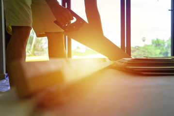 Closeup hand of man holds the manual saw and cuts the wooden in the house under construction with light of sunset.