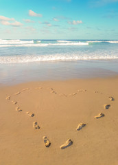 Footprints in the sand, heart shaped. Love traveling imprint on beach