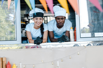 Selective focus of Asian girl and African American man in hats smiling from food truck