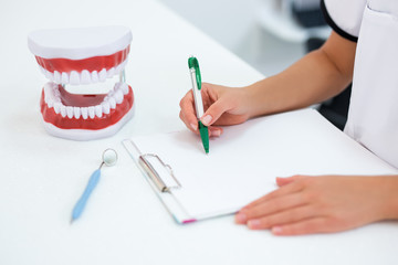 close up of female dentist's hands writing comething on clipboard
