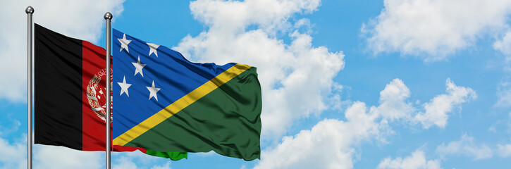 Afghanistan and Solomon Islands flag waving in the wind against white cloudy blue sky together....