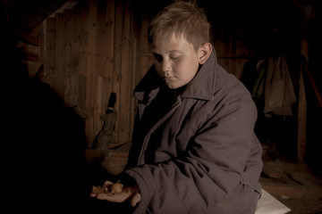 The boy is sitting in a chair. Dirty face, thick jacket. Dark background. The style of photography...