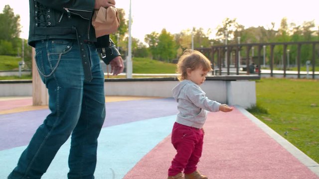 Funny baby walks over a dove in the park. Brutal father in biker jacket standing nearby.