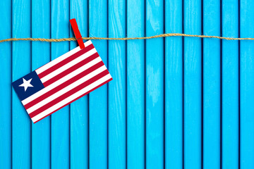 Flag of Liberia hanging on clothesline attached with wooden clothespins on aqua blue wooden background. National day concept.