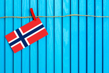 Flag of Norway hanging on clothesline attached with wooden clothespins on aqua blue wooden background. National day concept.