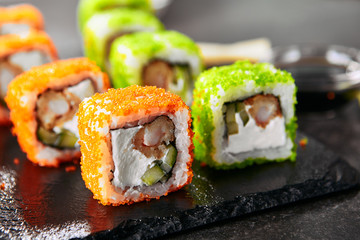 Macro shot uramaki sushi roll with rice, cream cheese, fried shrimp, cucumber, flying fish caviar and nori. Fresh colorful rolls in Japanese restaurant with chopsticks closeup