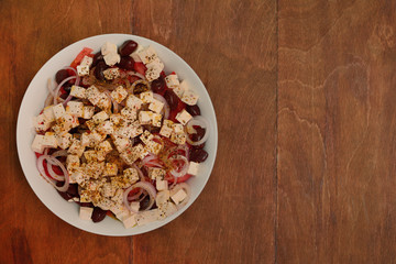 Greek salad in a large plate on a wooden table. View from above