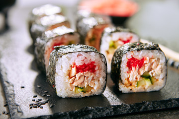 Macro shot of sushi roll in Japanese restaurant with chopsticks closeup. Sushi rolls with rice, fried salmon, flying fish caviar, cucumber and spicy sauce