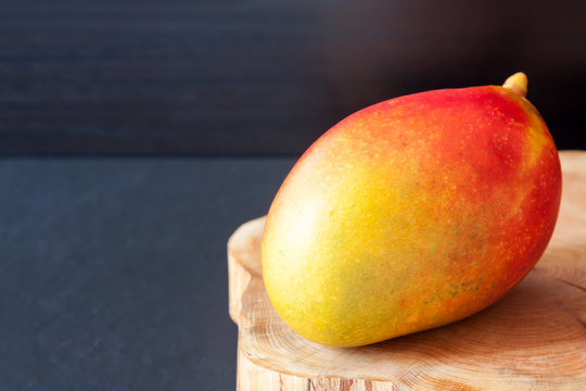 One fresh ripe red yellow mexican organic mango on wooden board dark background. Veggie tables concept image