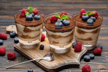 Classic tiramisu dessert with blueberries and strawberries in a glass cup on cutting board on wooden background