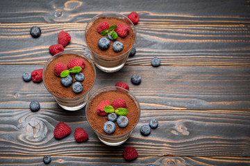 Classic tiramisu dessert with blueberries and strawberries in a glass cup on wooden background