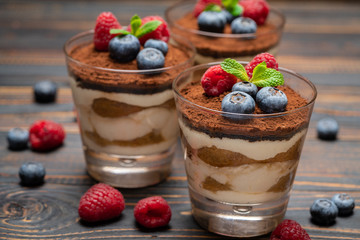Classic tiramisu dessert with blueberries and strawberries in a glass cup on wooden background