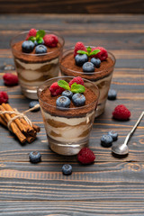 Classic tiramisu dessert with blueberries and strawberries in a glass cup on wooden background