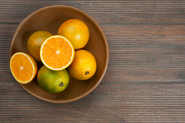 Oranges, vitamin C, in a clay bowl, brown.A half cut orange.Autumn wood color background.View from above.Space for text.