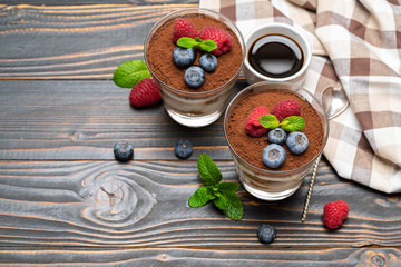 Classic tiramisu dessert with blueberries and strawberries in a glass cup on wooden background