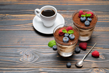 Classic tiramisu dessert with blueberries and strawberries in a glass cup and espresso coffee on wooden background