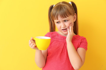 Little girl with sensitive teeth and cup of tea on color background