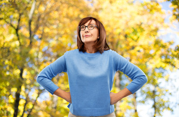 emotions and old people concept - displeased senior woman in glasses over autumn park background