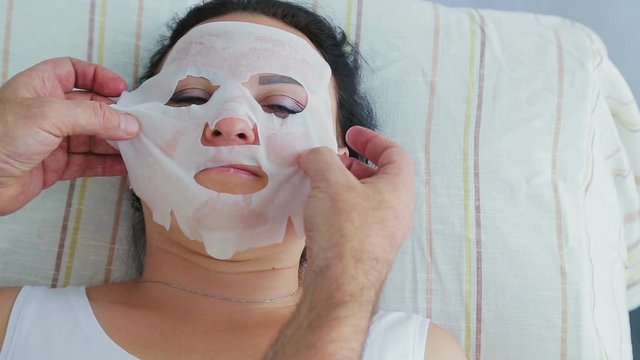A male cosmetologist applies a moisturizing face mask to a woman client in a spa salon