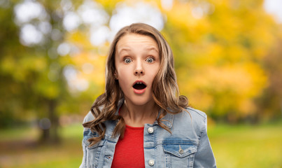 emotion, expression and people concept - surprised or shocked teenage girl with open mouth in denim jacket over autumn park background