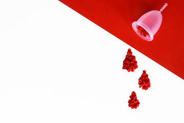 Red confetti arranged as a drops of blood from silicone menstrual cup. White and red background with copy space. Intimate hygiene for period.