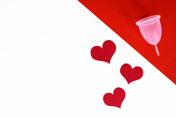 Top view of pink menstrual cup from medicinal silicone on red background. Red hearts on white background, with copy space. Concept of love your body.