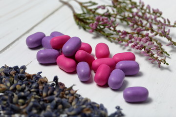 Dragee for refreshment of breath. Different color. Among the scattered flowers of lavender. Nearby are sprigs of heather. Lying on a white surface.