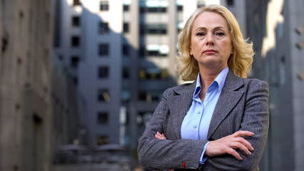 Aged female boss looking camera folded arms on office building background, job