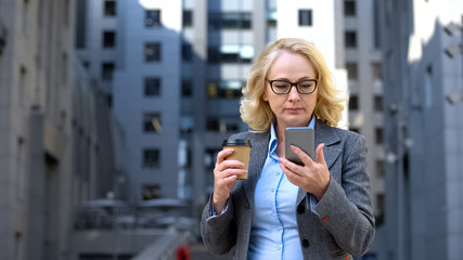 Serious head of department reading smartphone business news holding coffee cup