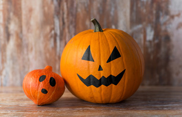 halloween decorations concept - pumpkin and red kuri squash with scary faces on wooden background
