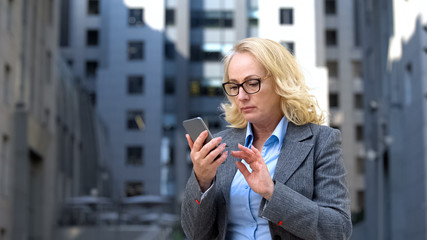 Serious aged lady boss checking meeting schedule app by smartphone, internet