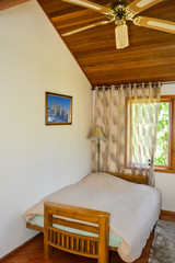Small lightful bedroom with curtains on windows and rug on the floor.