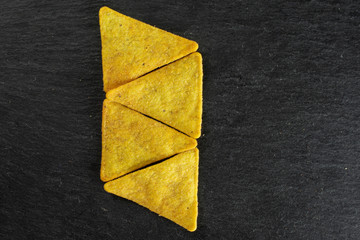 Group of four whole cheese tortilla chips in row flatlay on grey stone