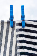 Dishcloths drying on clothesline. Closeup of two horizontal and vertical striped grey black white towels drying on a line with two large blue clothespins against a grey cloudy sky. Vertical image.