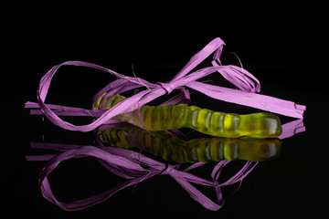 One whole colourful jelly worm candy tied by violet ribbon isolated on black glass