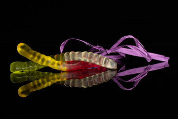 Obraz na płótnie Canvas Group of two whole bright colourful jelly worm candy tied by violet ribbon isolated on black glass