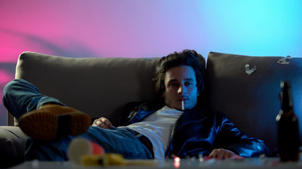 Intoxicated man with cigarette lying on coach, enjoying home party, addiction