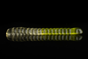One whole green white colourful jelly worm candy isolated on black glass