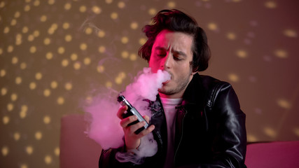 Relaxed hipster man vaping e-cigarette at rave party in night club, bad habits