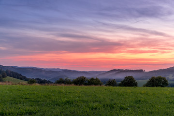 Morning sunrise in Beskyd area colored dark sky with clouds and fresh fog covering grass around mountains and hills behind in the valley.