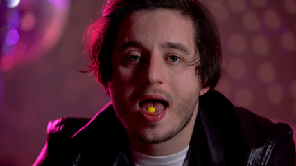 Guy holding narcotic pill on tongue in night club, unhealthy recreational drugs
