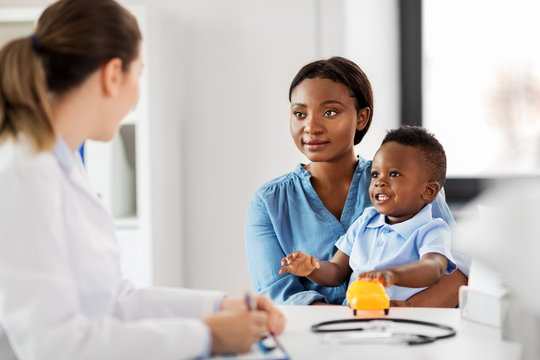 medicine, healthcare and pediatry concept - happy african american mother with baby son and caucasian doctor at clinic