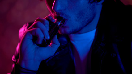 Male criminal vaping e-cigarette in night club darkness, unhealthy habit