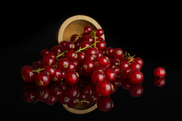 Lot of whole fresh red currant in bamboo bowl isolated on black glass