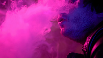 Male exhaling smoke from e-cigarette, relaxing on party in night club, habit